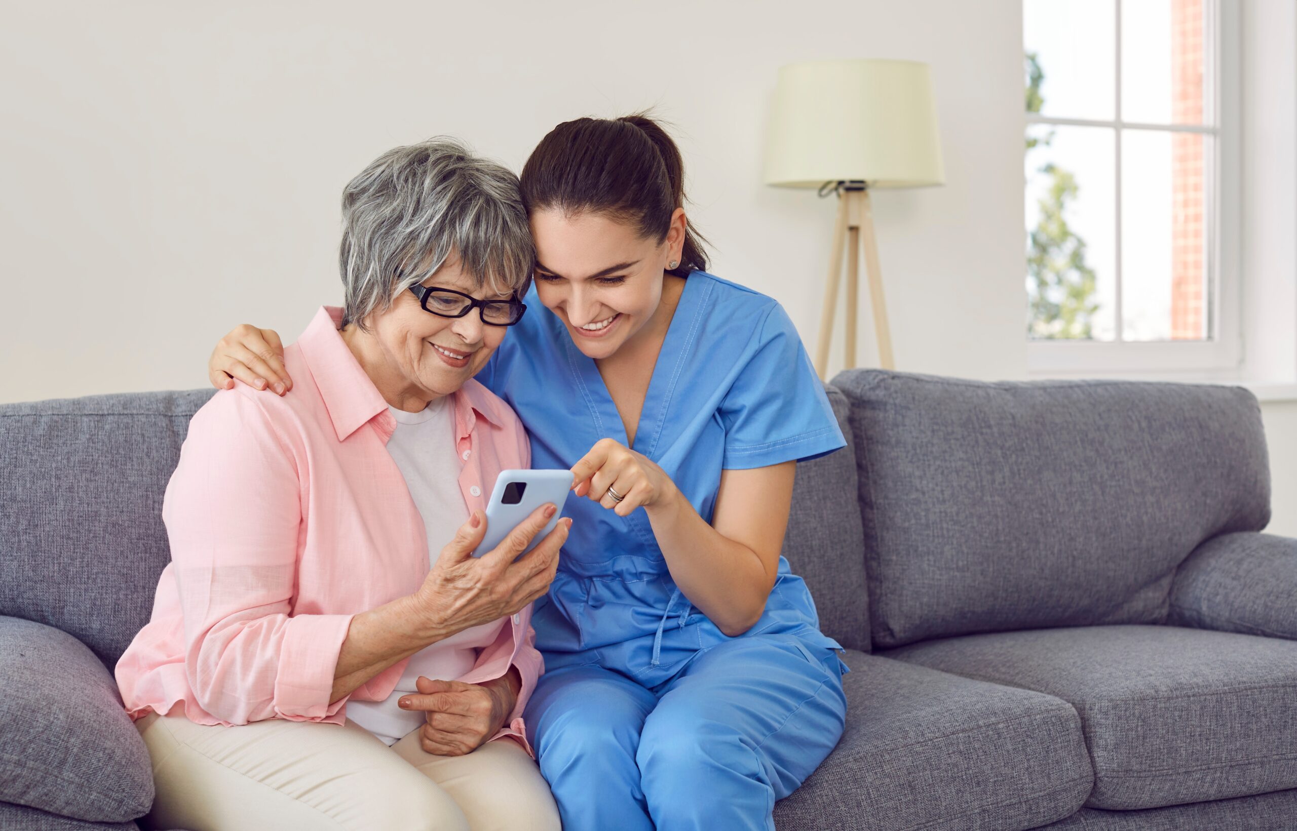 An assisted living caregiver demonstrating smart technology features on an older adult resident's phone.