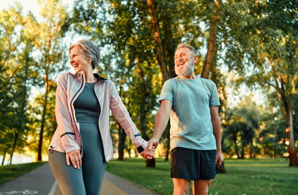 An older adult couple happily holding hands while walking in a park.
