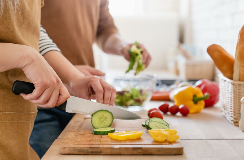 A close-up of two people's hands chopping veggies and prepping a salad.
