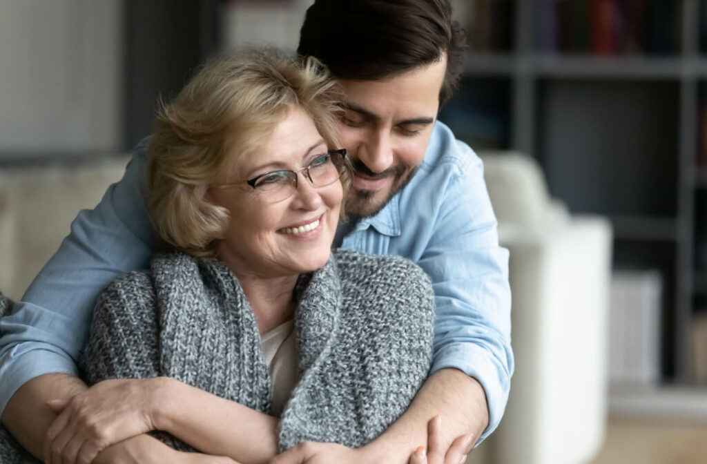 A senior woman with his son sitting on the couch, smiling and hugging each other.