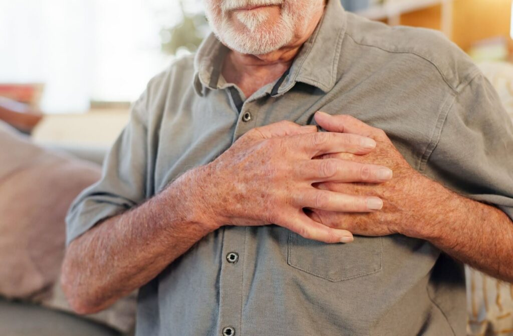 An older adult clutches their hands over their chest in discomfort, signaling the potential of a medical emergency