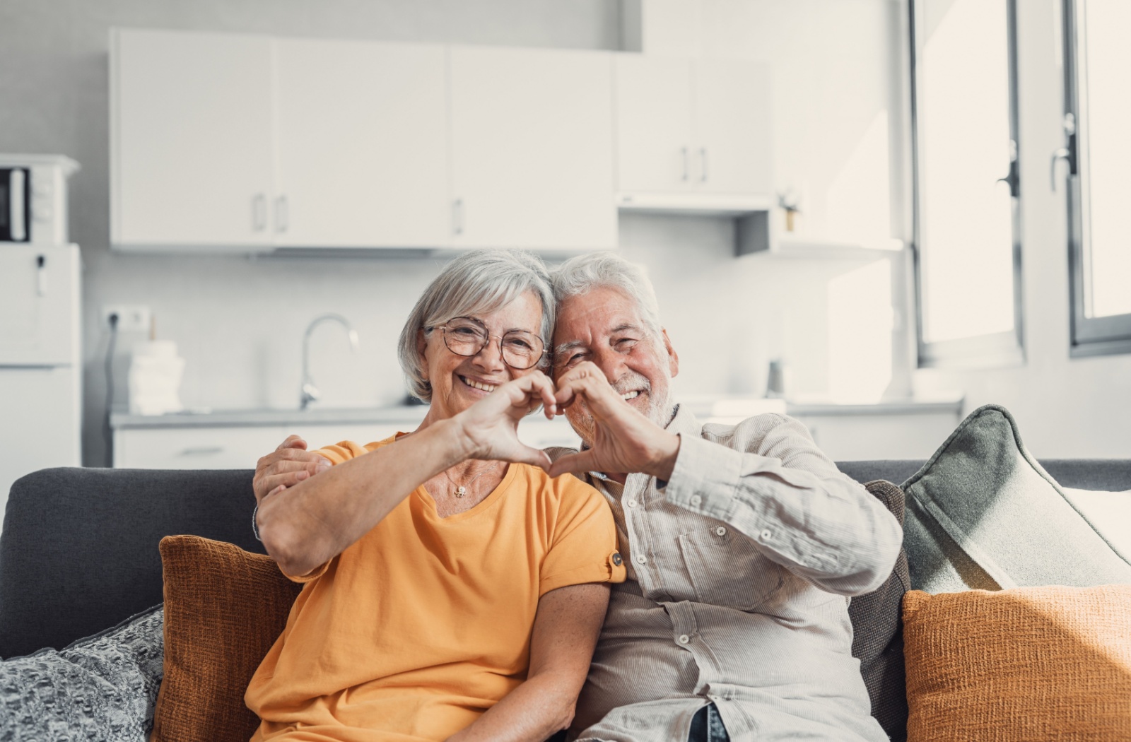 An older adult couple makes a heart shape with their hands, smiling together.